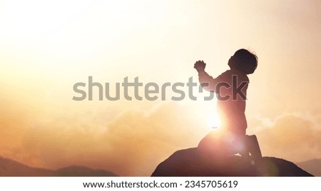 Child Christian earnestly praying to God and Jesus with both hands together under the red sunset sky and bright sunlight
