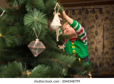 child in a Christmas elf costume is decorating an artificial tree in house. Cozy festive atmosphere. Waiting for holiday. Preparing for New Year