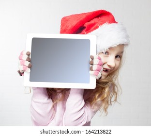 Child In Christmas Hat With Tablet Pc. Happy Girl Showing Tablet Screen