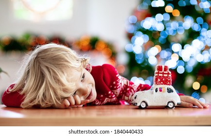 Child with Christmas present. Kid with Xmas gift. Little boy playing with a toy car under Christmas tree. Decorated home for winter holidays. Celebration with children. Kids play.