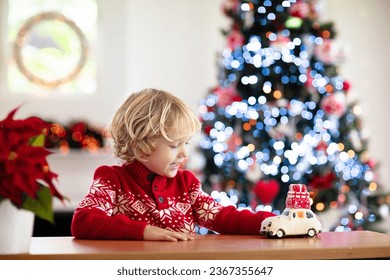 Child with Christmas present. Kid with Xmas gift. Little boy playing with a toy car under Christmas tree. Decorated home for winter holidays. Celebration with children. Kids play. - Powered by Shutterstock