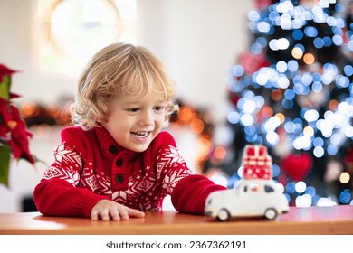 Child with Christmas present. Kid with Xmas gift. Little boy playing with a toy car under Christmas tree. Decorated home for winter holidays. Celebration with children. Kids play. - Powered by Shutterstock