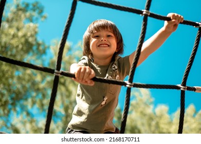 A child climbs up an alpine grid in park playground hot summer day  children's playground in public park  entertainment   recreation for children  mountaineering training 