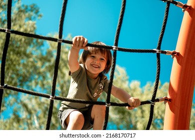 A child climbs up an alpine grid in a park on a playground on a hot summer day. children's playground in a public park, entertainment and recreation for children, mountaineering training. - Shutterstock ID 2168170717