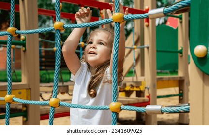 A child climbs up an alpine grid in a park on a playground on summer day. children's playground in a public park, entertainment and recreation for children - Shutterstock ID 2341609025