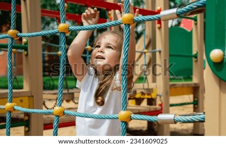 A child climbs up an alpine grid in a park on a playground on summer day. children's playground in a public park, entertainment and recreation for children