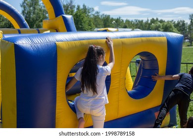 A Child Climbs An Inflatable Slide. Obstacle Course For Children. Inflatable Playground. The Child Clings To Climb The Hill. Entertainment And Recreation For The Child.