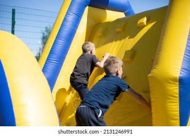 A Child Climbs An Inflatable Slide. Obstacle Course For Children. Inflatable Playground. The Child Clings To Climb The Hill. Entertainment And Recreation For The Child.