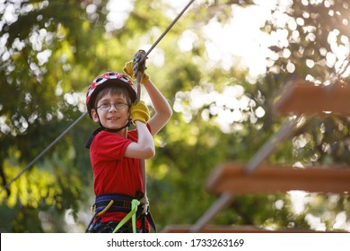 Child Climbs In A Rope Park. Boy In Adventure Park Having Fun In High Wire Park. Toddler Boy On A Ropes Course. Male Toddler On Zip Line. Boy Having A Fun On Climbing Frame. Boyscout On A Tree. Summer