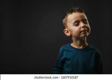 Child Closed His Eyes And Dreams Of Not Looking At Camera Isolated On Blank Gray Studio Background, Young Boy Posing For Portrait.