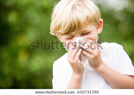 Child with a cold sneezing and holding tissue on his nose