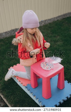 Child concentrating, stringing small beads into a bracelet or necklace, engaging in creative activities at home