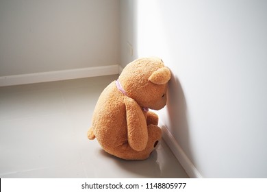 Child concept of sorrow. Teddy bear sitting leaning against the wall of the house alone, look sad and disappointed.            