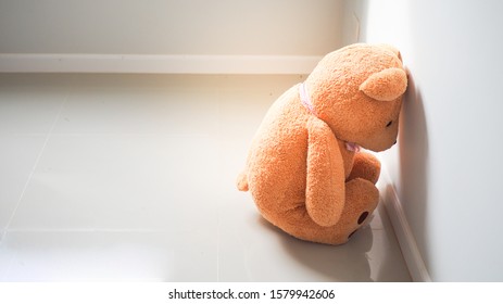 Child concept of sorrow. Teddy bear sitting leaning against the wall of the house alone, look sad and disappointed.