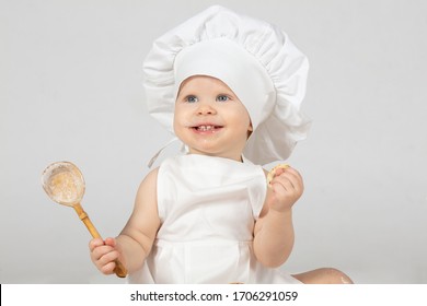Child cook. Beautiful little girl in cook clothes with a big spoon. The child is one year old. Funny baby is laughing. Little chef. The concept of cooking food.
