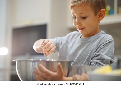 Child cooking at the kitchen. White boy stirring dough for a cookie. Kid is mixing ingredients for a cake in the steel bowl. 8 years old child cooking food at home. 