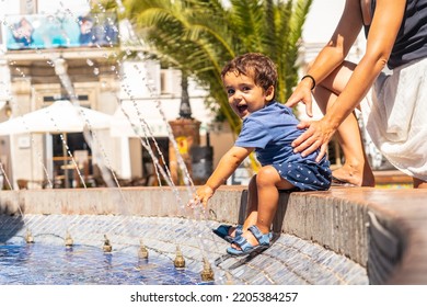 A Child Cooling Off In The Water Fountain In The Plaza De España In Vejer De La Frontera, Cadiz.