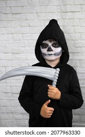 Child With A Costume Of The Grim Reaper With A Scythe And With A Make-up Face