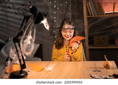 The Child Create A Greeting Packaging On Halloween Pumpkin Paper At Home In The Evening. Children's Art Project, A Craft For Children. Copy Space