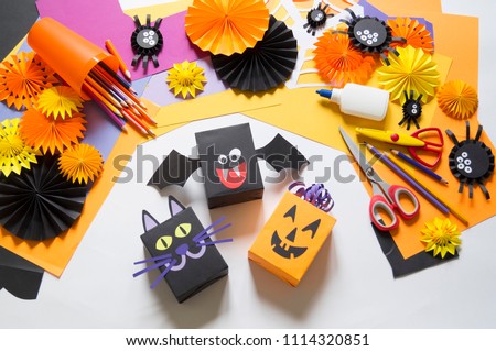The child creates a gift box of a black cat,bat and pumpkin. A party for Halloween. Children's hands make a master class. Craft for kids. Materials for creativity of orange, purple and black colors.