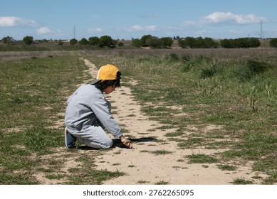 Child crouching and exploring a dirt path in a rural landscape
