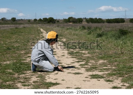 Child crouching and exploring a dirt path in a rural landscape