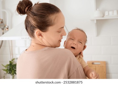 Child crying in mommy's arms loving young mother hugging and comforting her little daughter or son mom calming child in kitchen interior - Powered by Shutterstock