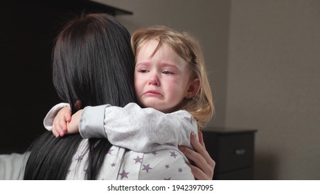 Child is crying in room in the arms of his mother. A loving young mother hugs and comforts her little daughter. Mom calms child. Family mother and baby with tears in their eyes emotionally embrace - Shutterstock ID 1942397095