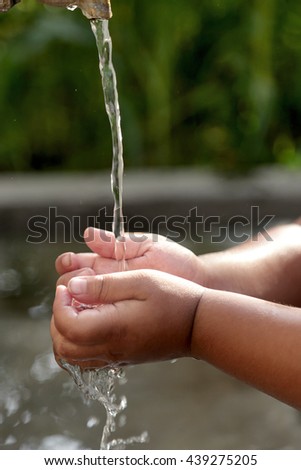 A child cups a small stream of slow flowing water from a single tap