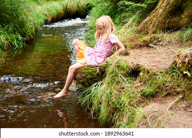 Child cute blond girl playing in the creek. Gril walking in forest stream and exploring nature. Summer children fun. Children summer activities