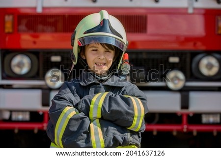 Child, cute boy, dressed in fire fighers cloths in a fire station with fire truck, childs dream