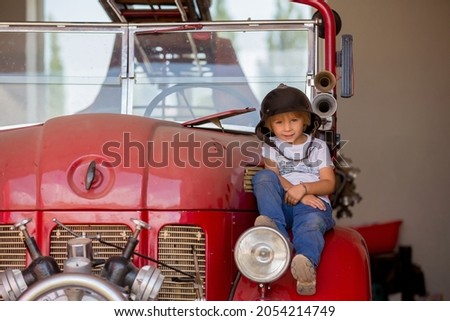 Child, cute boy, dressed in fire fighers cloths in a fire station with fire truck, childs dream