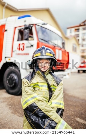 Child, cute boy, dressed in fire fighers cloths in a fire station with fire truck, childs dreamed profession.
