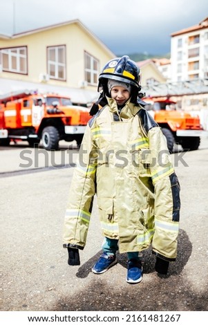 Child, cute boy, dressed in fire fighers cloths in a fire station with fire truck, childs dreamed profession.