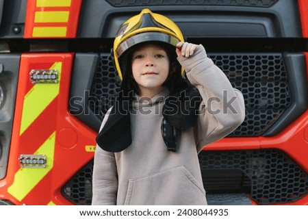 Child, cute boy, dressed in fire fighers cloths in a fire station with fire truck, childs dream.