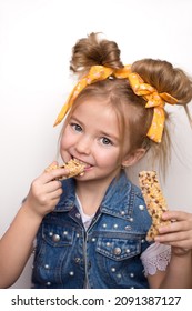 the child is a cute girl holding a granola bar in her hand, a healthy snack for breakfast. Beautiful smile of a child biting a bar of rice balls and berries