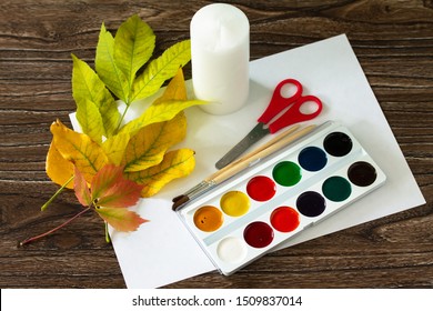 The Child Cuts Out Autumn Leaves With A Candle And Watercolors On Wooden Background. Crafts From Paper For Children. Children's Art Project. 