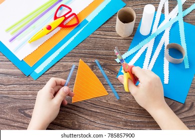 The child cuts out the details of a paper boat, congratulations concept of Father's Day. Glue, scissors and paper on a wooden table. Children's art project craft for kids. Craft for children. - Powered by Shutterstock