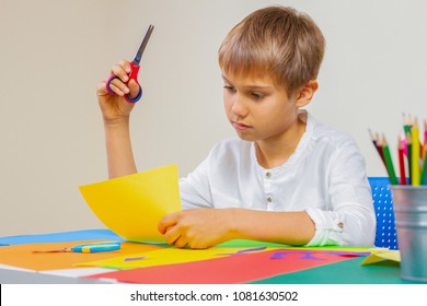 Child Cutting Colored Paper With Scissors At The Table