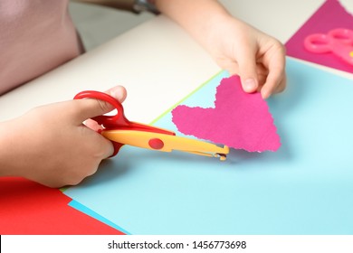 Child Cutting Out Paper Heart With Craft Scissors At Table, Closeup