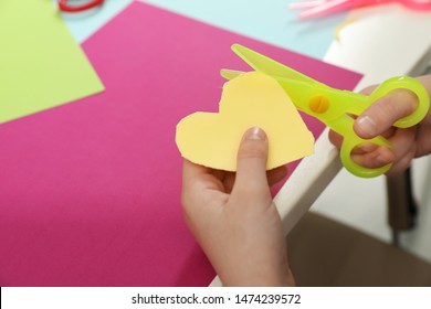 Child Cutting Out Paper Heart With Plastic Scissors At Table, Closeup. Space For Text