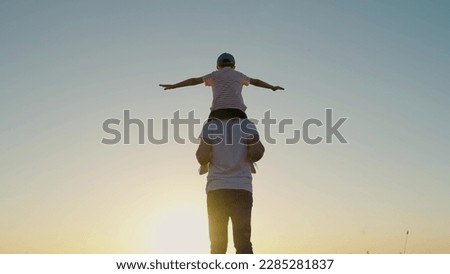 Child dad, fantasize, kid aviator sits on his fathers shoulders, against sky. Father Son play together in front of sun, dream, fly. Happy family, childhood dream. Boy plays pilot airplane, hands wings