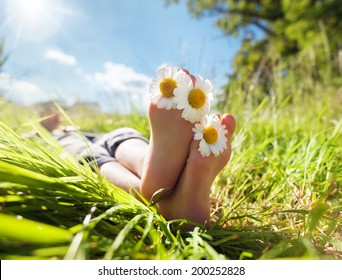 Child with daisy between toes lying in meadow relaxing in summer sunshine