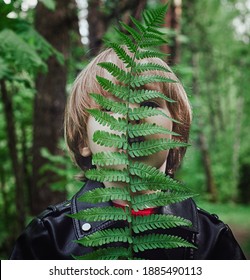 A Child In A Dark Forest Is Covered By A Fern Leaf. Child In A Black Leather Jacket In The Forest Fashionable Trendy Concept Deep Matte Shadows