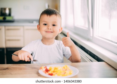 Child Day In The Kitchen Eating An Omelet With Sausage And Ketchup In A White T-shirt