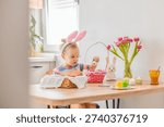 Child decorates Easter eggs in a bright room with flowers and cute decorations during a holiday activity at home