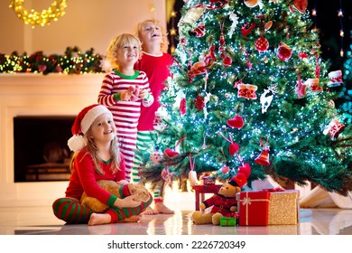 Child decorating Christmas tree at home. Little boy and girl in pajamas with Xmas ornament. Family with kids celebrate winter holidays. Kids decorate living room and fireplace for Christmas.