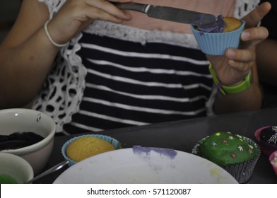 Child Decorating A Cupcake While Sitting At A Table