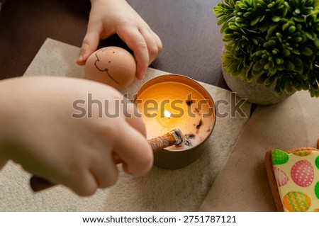 Child decorating Easter egg using traditional wax technique with candle and tool