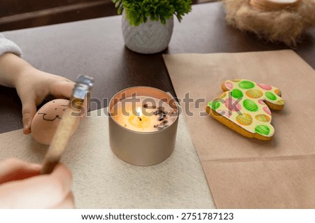 Child decorating Easter egg using traditional wax technique with candle and tool